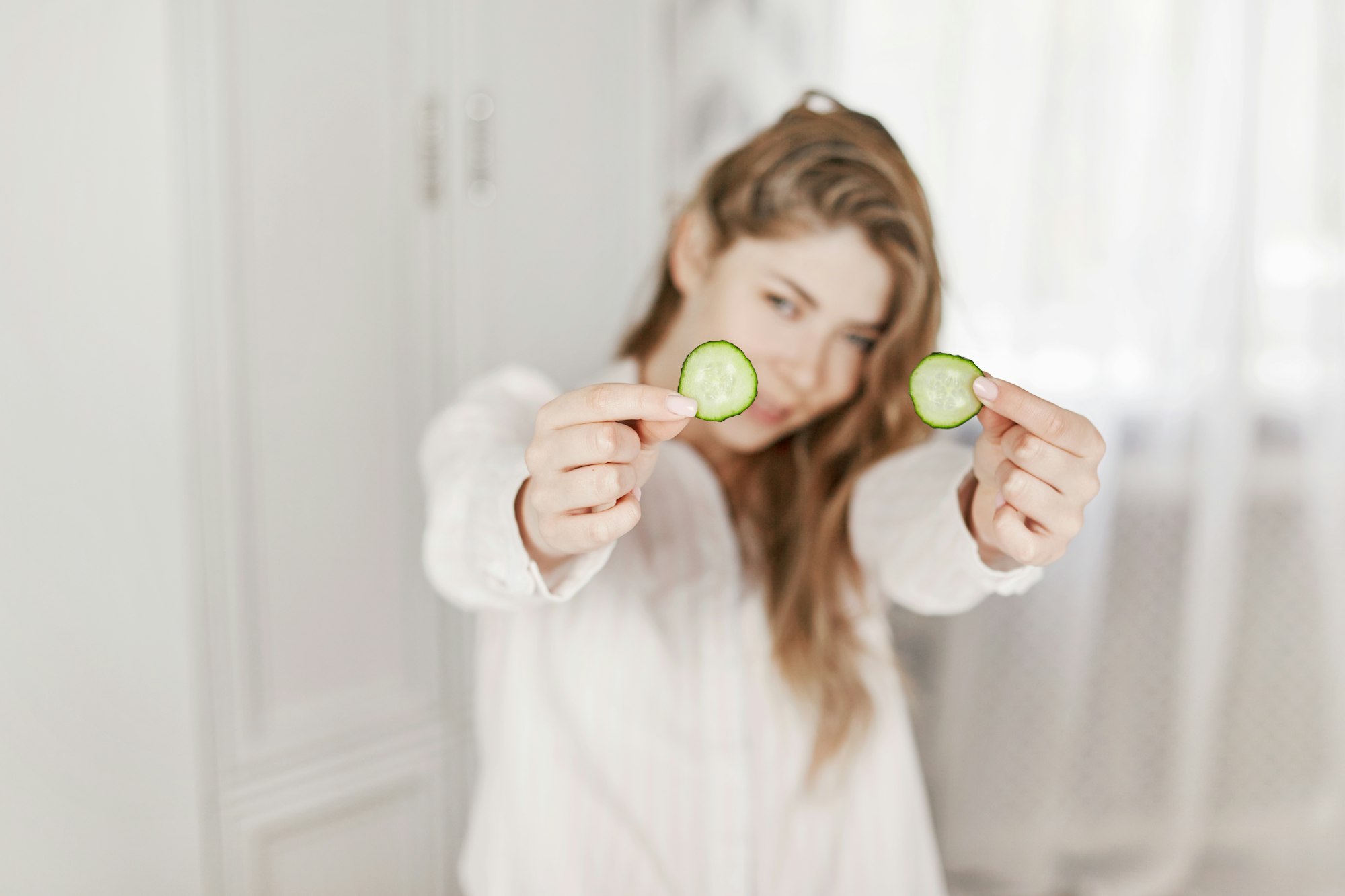 A cheerful girl holds cucumber slices in her hands for a face mask. Skin care