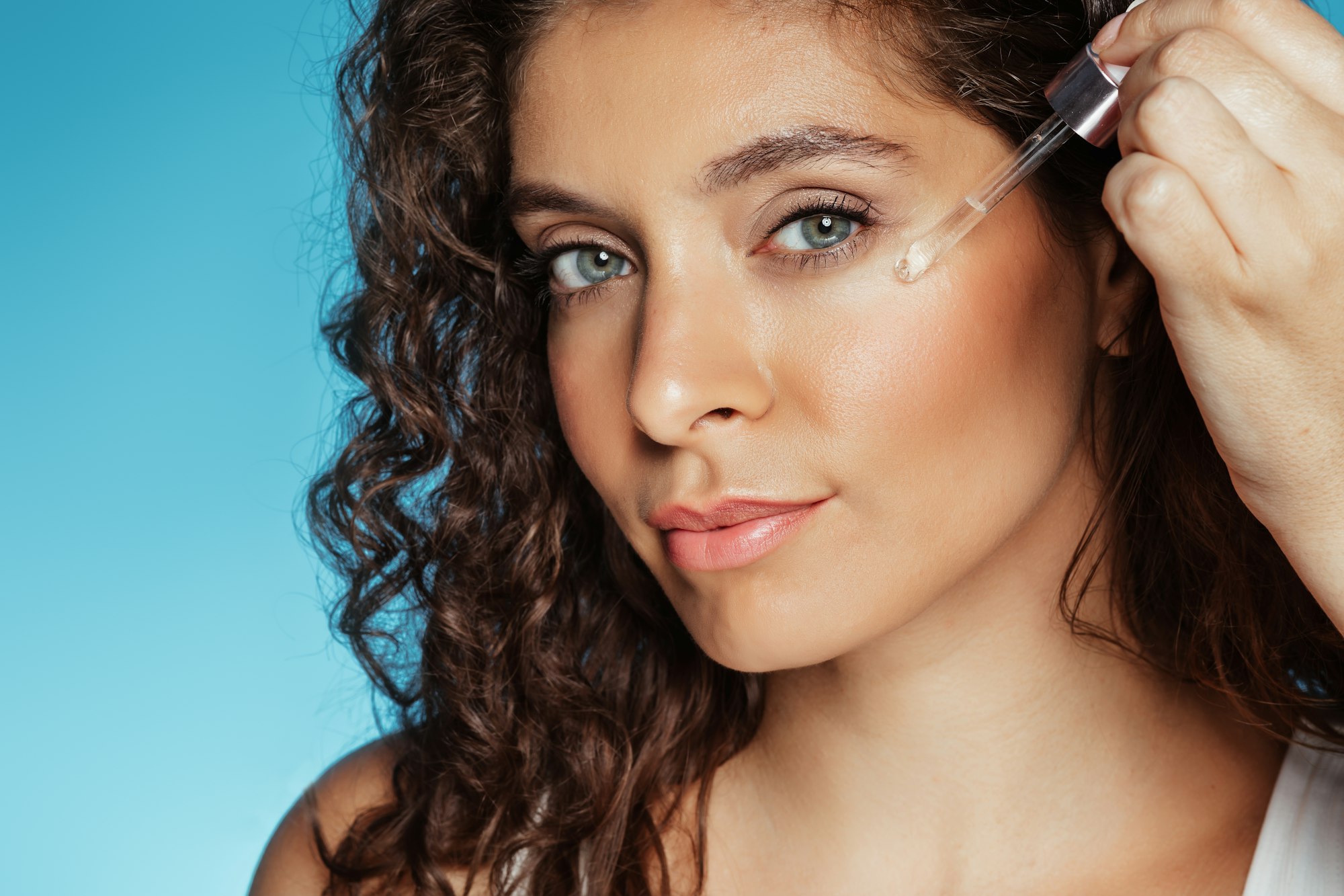 Calm millennial european curly lady applying serum to face skin