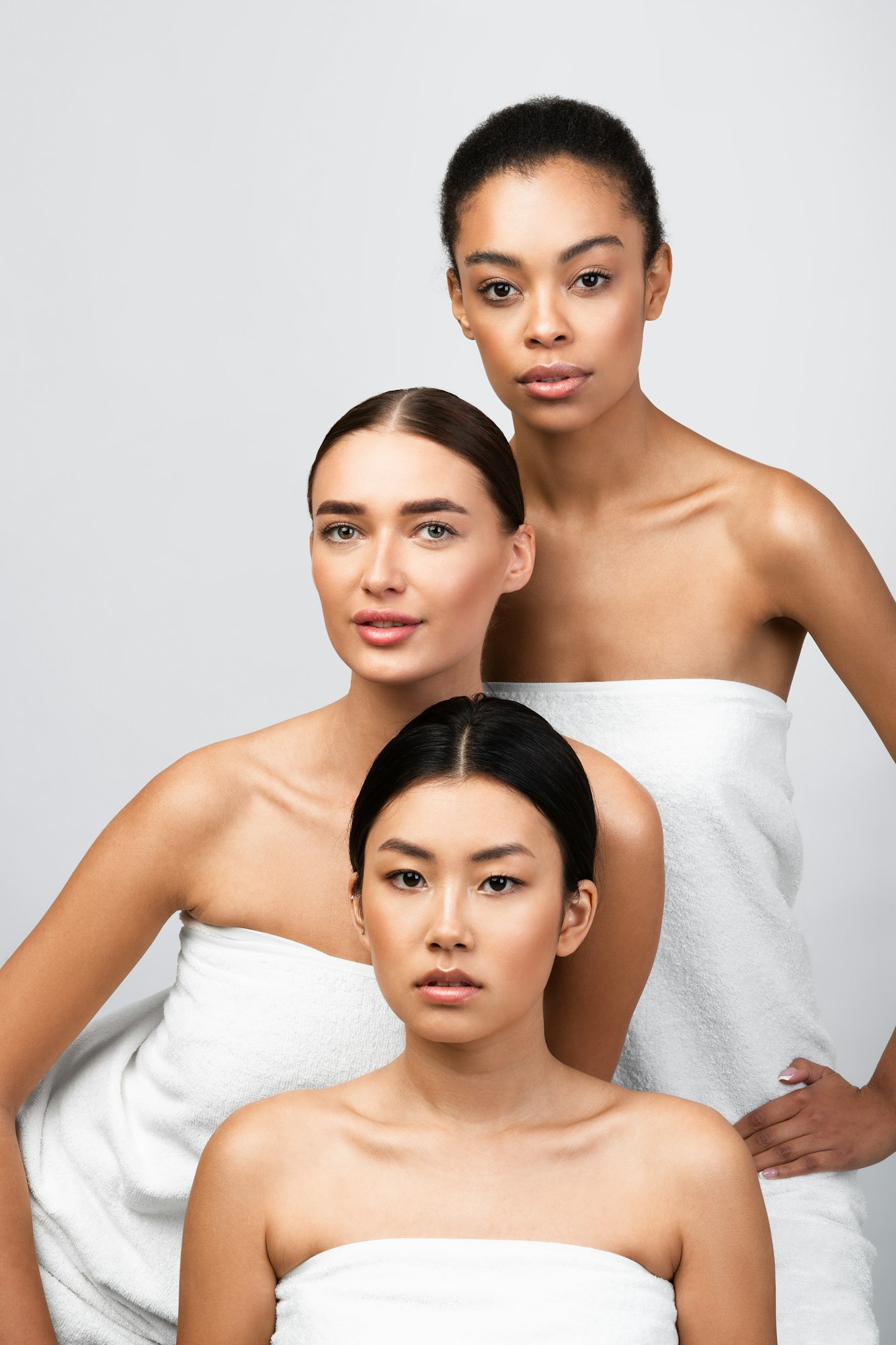 Three Women Posing Wrapped In Towels Over Gray Background, Vertical